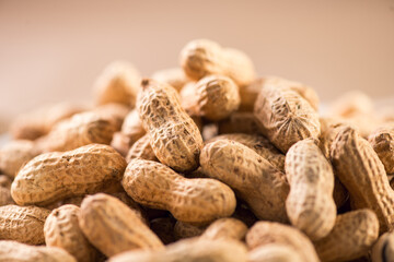 Peanuts. Unshelled nuts close up, over beige background. Roasted pile of peanuts in shell. Organic vegan, vegetarian food. Healthy nutrition concept.