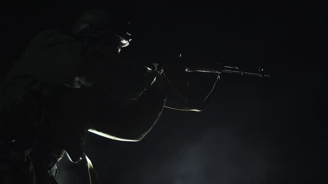 SLOW MOTION - Silhouette of military soldier, infantryman with weapons at night. Warrior shoots, holding machine gun, darkness, night background. Flash from a shot from a firearm on a black background