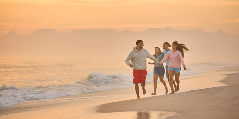 Couple With Friends On Vacation Holding Hands Running Along Beach Shoreline At Dawn