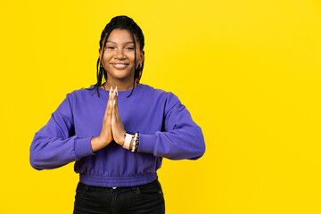 An afro woman making gesture of gratitude or asking for forgiveness smiling confident in purple sweater on yellow background. - obrazy, fototapety, plakaty