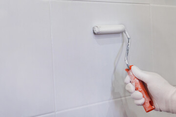 Painting tiles in the kitchen in the bathroom, white paint with a roller. Hand in glove with roller
