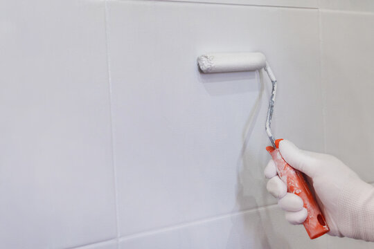 Painting tiles in the kitchen in the bathroom, white paint with a roller. Hand in glove with roller