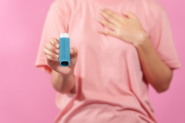 A professional image featuring a female hand holding an asthma inhaler with fingers against a soft...