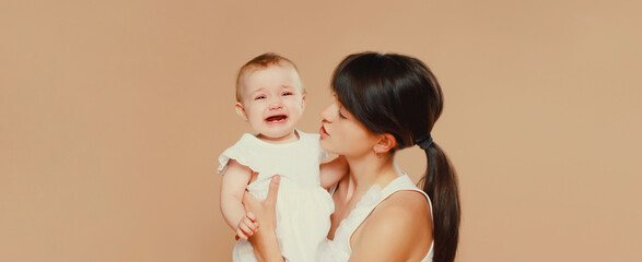 young mother holding crying baby on studio background