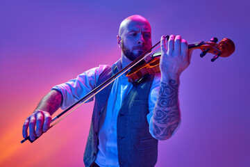 Bald man in classical clothes, with tattoo, musician playing violin against gradient purple...