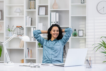Fototapeta na wymiar A relaxed Hispanic woman takes a break while working remotely in her bright home office, embodying work-life balance.