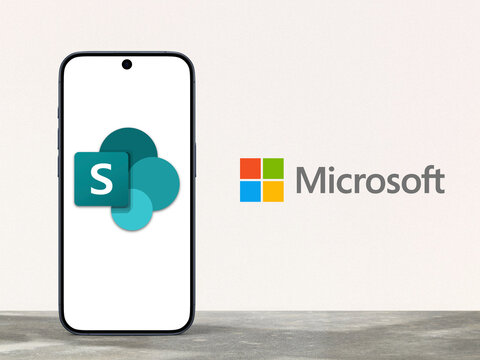 Microsoft Sharepoint logo is displayed on a modern smartphone standing on a desk, Microsoft logo next to it, collaboration Microsoft 365, team management, file sharing