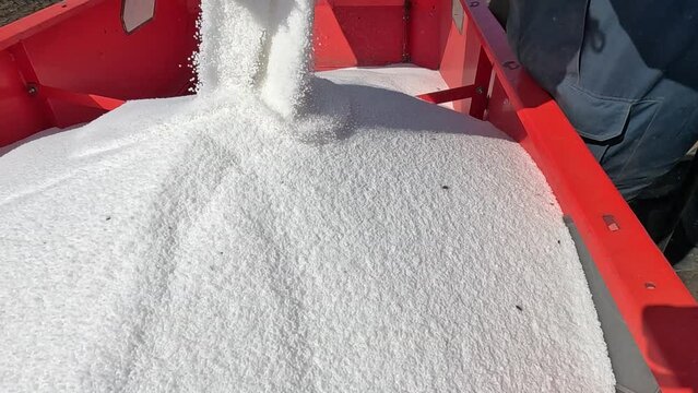 Pouring mineral fertilizer in granules into the fertilizer spreader, slow motion. Farmer pouring fertilizer from large sacks. Proper growth of plants requires a balance of nutrients found in the soil