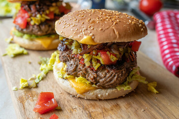 Big Cheeseburger with onions, pickles, tomatoes on a wooden cutting board
