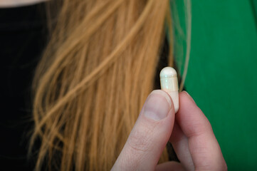 Naklejka premium Kobieta trzyma kapsułkę z witaminami na mocne włosy przy swoich blond włosach 