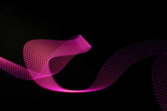 Pink and purple neon glowing wave of light as curls with dotted stripes on black background, pattern. Abstract background with motion light effect, light painting in disco party style.