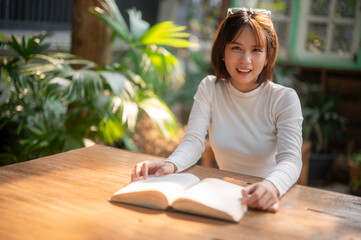 A young woman deeply absorbed in reading a book, bathed in warm sunlight at a rustic outdoor table,...