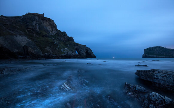 The ancient hermitage of San Juan de Gaztelugatxe stands guard over a misty seascape as twilight descends upon the Basque coastline