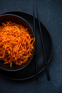 Grated carrot salad in a black bowl with chopsticks