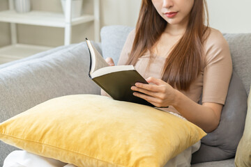 Having relaxing weekend concept, happy beautiful asian young woman, girl sitting in cozy sofa. Close up hand open reading a book beside the window after get up in morning lifestyle at home and comfort