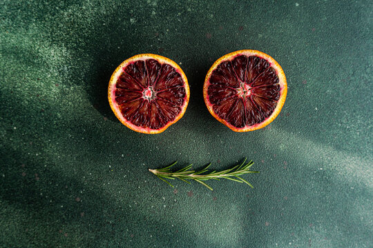 Fresh blood oranges and rosemary on green surface