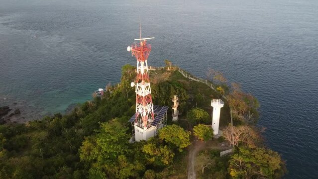 Aerial view of a small lighthouse and cell tower on the seashore. Top view of a cell phone tower on the edge of a cliff on a tropical island.