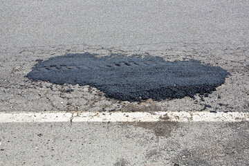 Old damaged and worn asphalt road with pothole filled with new bitumen - obrazy, fototapety, plakaty
