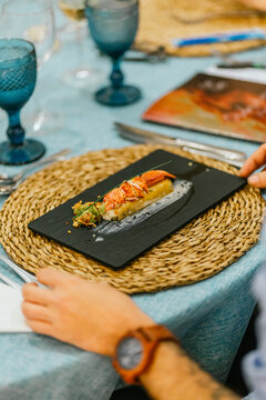 A gourmet lobster dish beautifully presented on a black slate, surrounded by an intricate table setting with a nautical theme