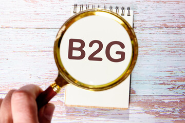 Business concept. The letters B2G through a magnifying glass in a notebook against the background of old boards