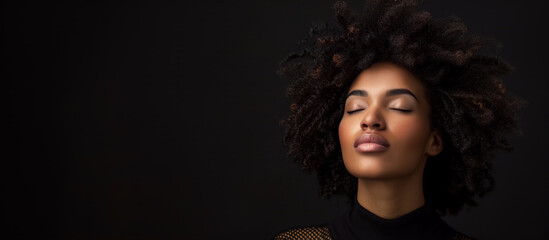 Fototapeta premium A close-up portrait of a brunette black woman model close the eye with long dark hair and glamorous makeup on black background in studio.