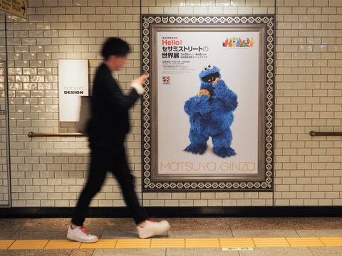 TOKYO, JAPAN - April 2, 2024: Person passing a poster advertising a Sesame Street exhibition being held at Matsuya department store in Ginza. Some motion blur.