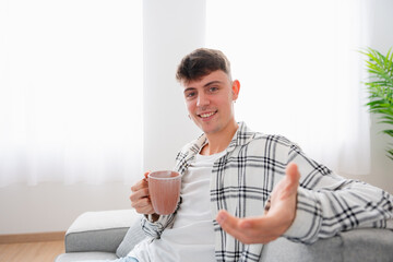 Portrait with copy space of a man gesturing an invitation to drink coffee in the sofa