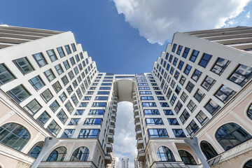 view from below into blue sky with clouds of large modern skyscraper residential complex with arch - obrazy, fototapety, plakaty