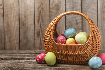 Easter basket filled with colorful eggs and a bouquet of tulips on a textured wooden table. Easter celebration concept. Colorful easter handmade decorated Easter eggs. Place for text. Copy space