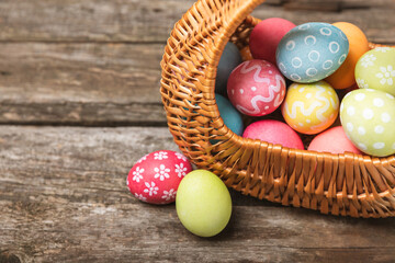 Easter basket filled with colorful eggs and a bouquet of tulips on a textured wooden table. Easter celebration concept. Colorful easter handmade decorated Easter eggs. Place for text. Copy space