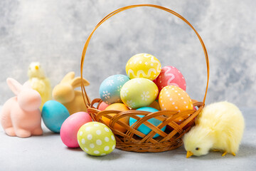 Easter basket filled with colorful eggs and a bouquet of tulips on a textured wooden table. Easter...