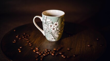 Coffee cup with flowers on it on a dark brown table with coffee beans near it