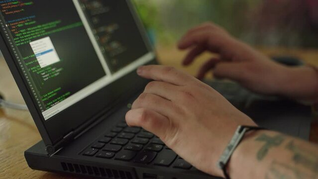 Tattooed programmer types code on laptop, debugging software project. Pro developer engages in coding at work desk, tech career focus. Expert creates app, artificial intelligence development. Slowmo