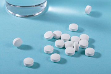 Herbal and Vitamin white pills healthy food freely laid near glass of water on light blue background for healthy eating in daily life
