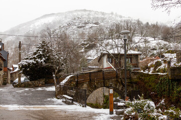 un puente de piedra sobre un rio de un pueblo de montaña nevado
