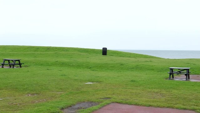 St Bees seaside resort on Irish sea of Cumbrian coast on overcast rainy day, 180 degrees panning shot includes coastal cafe and other buildings, picnic tables on the grass, sea, some incidental people