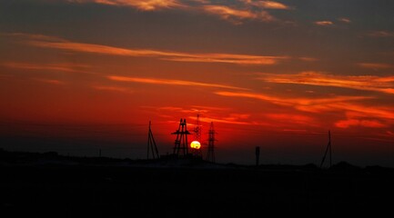 Scenic view of a vibrant red sunset in the cloudy sky with silhouettes of electric towers