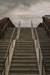 Vertical shot of steps leading onto a bridge with wooden railings under a dark sky on a gloomy day