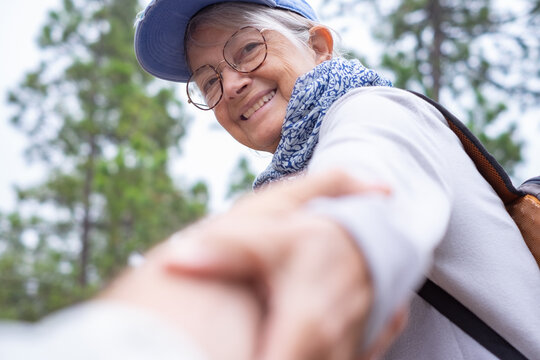 Portrait of happy active senior woman walking in pine forest giving hand to someone else to rise. Healthy lifestyle and freedom concept - Powered by Adobe