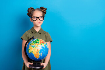 Photo of minded schoolchild hold round globe look empty space answer homework wear t shirt isolated...