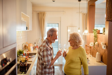 Happy senior couple toasting with wine at home kitchen