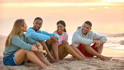 Obraz premium Young Couple With Friends In Casual Clothing On Vacation Sitting On Beach Watching Sunrise Together