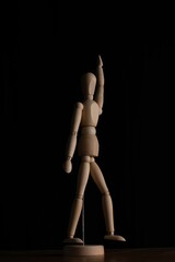 Vertical closeup of a wooden marionette figure with its arm up against a black background