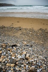 Vertical shot of a coast during a foamy tide with pebbles on the sand