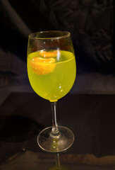 A glass of lemonade with floating pieces of tangerine on a black background.