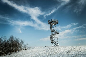 Viewing tower with spiral staircase on the top of snowy hill under blue cloudy sky