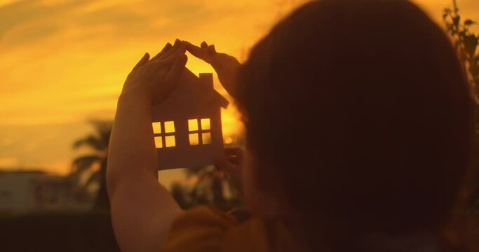 Young people secure cut out house dreaming about loving private home for family. Symbol of shared dreams for future marriage life. Paper house hands family, sun shines in window closeup.House at