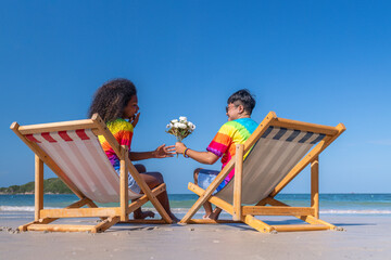 Romantic happiness couple LGBTQ lover sitting on beach chair giving flower show happiness with...