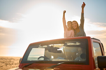 Couple With Friends On Vacation Driving Car On Road Trip Adventure To Beach Standing Up Through Roof