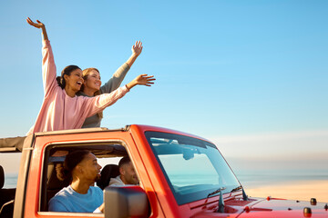 Couple With Friends On Vacation Driving Car On Road Trip Adventure To Beach Standing Up Through Roof